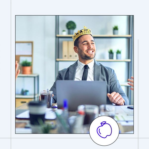 a man sitting in front of a laptop smiling wearing a crown